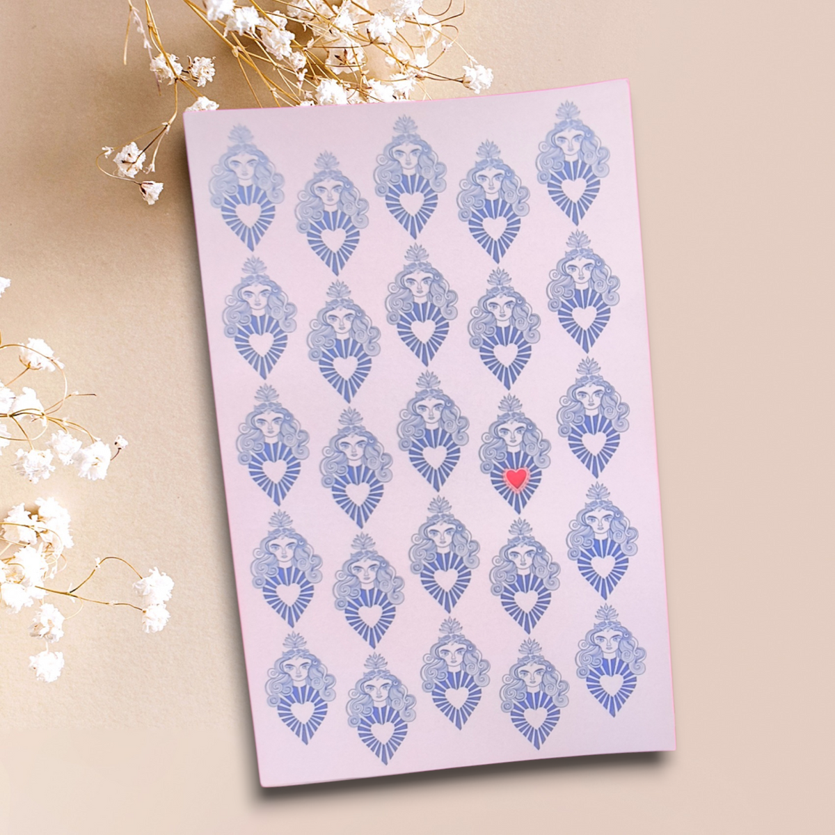 Libreta con patrón de rostros y corazones azules sobre fondo rosado, con un corazón rojo
